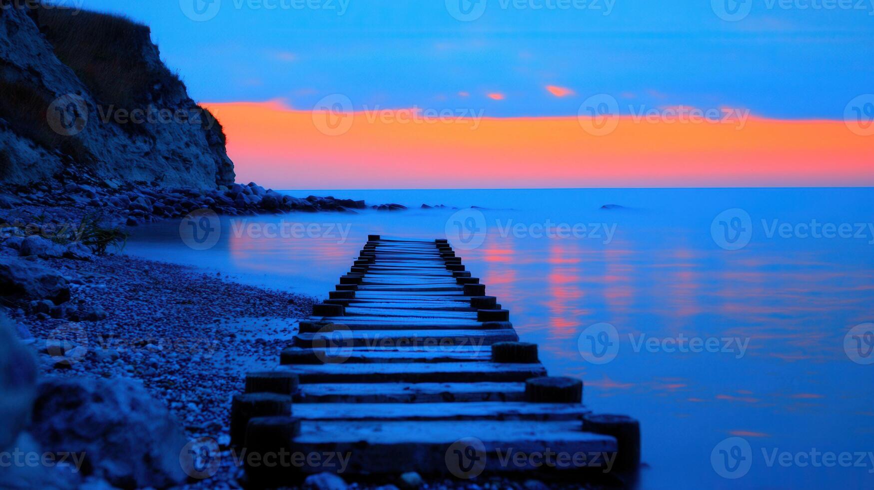 Serene Sunset Seascape Wooden Dock Leading to Calm Ocean Waters Peaceful Evening Coastal Scene with Rocky Shoreline photo
