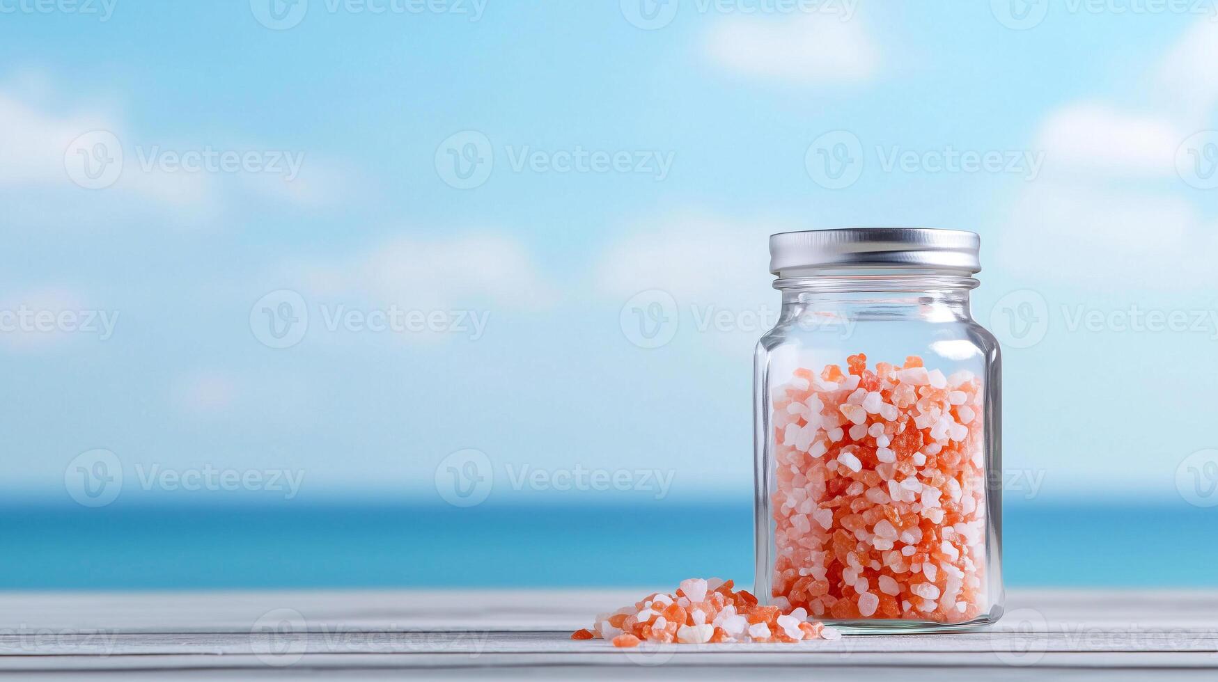 A beautifully arranged jar filled with vibrant pink and white sea salt sits on a wooden surface, with a serene ocean backdrop, perfect for culinary and wellness themes. photo