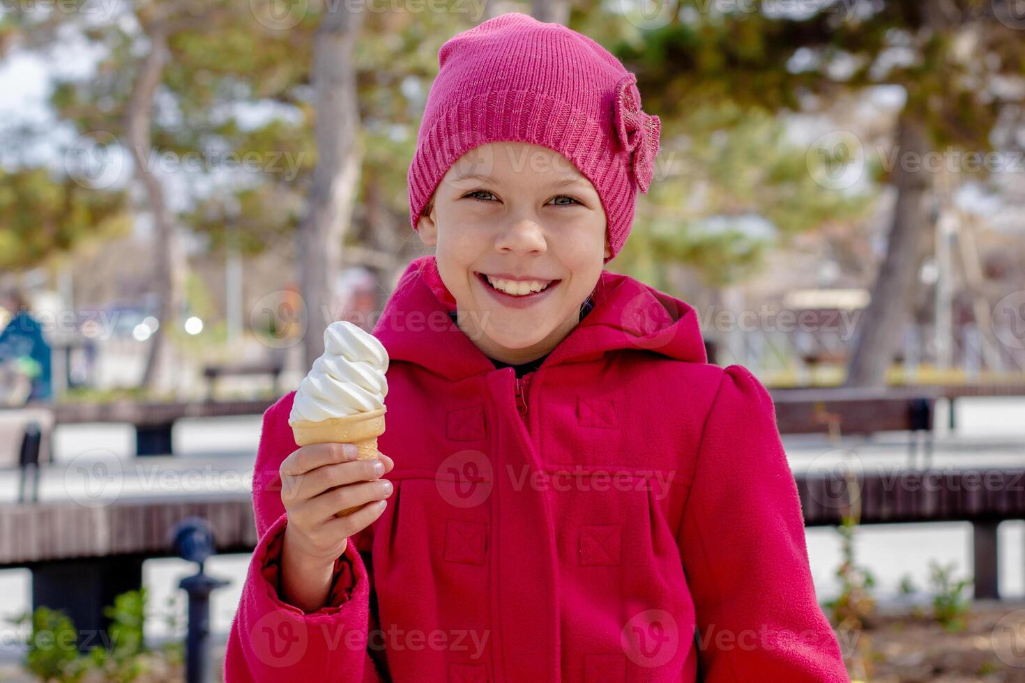 Portrait of happy and smiling caucasian little girl of 8 9 years holding ice cream cone outside in red coat and hat photo