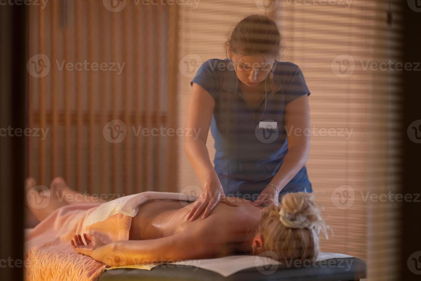 Relaxing Back Massage in a Spa Setting. A professional massage therapist in a blue uniform provides a relaxing back massage to a client lying on a massage table. photo