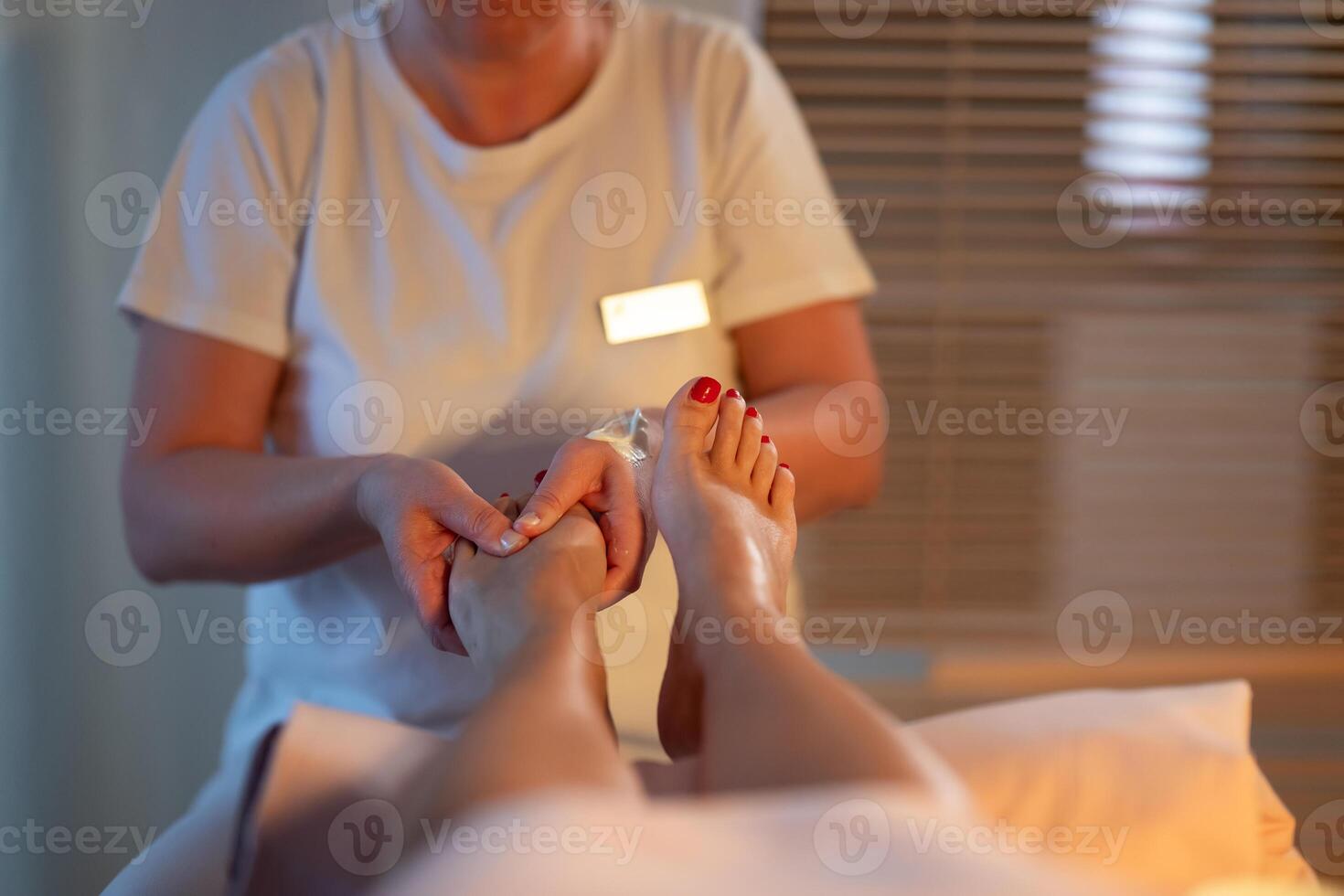 Foot Massage Therapy in a Relaxing Spa Setting. A professional massage therapist in a white uniform provides a soothing foot massage to a client in a calm and serene spa environment photo