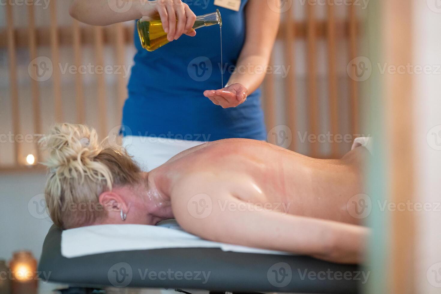 A professional massage therapist pours aromatic oil into their hands, preparing for a relaxing and rejuvenating massage session in a serene spa setting. photo