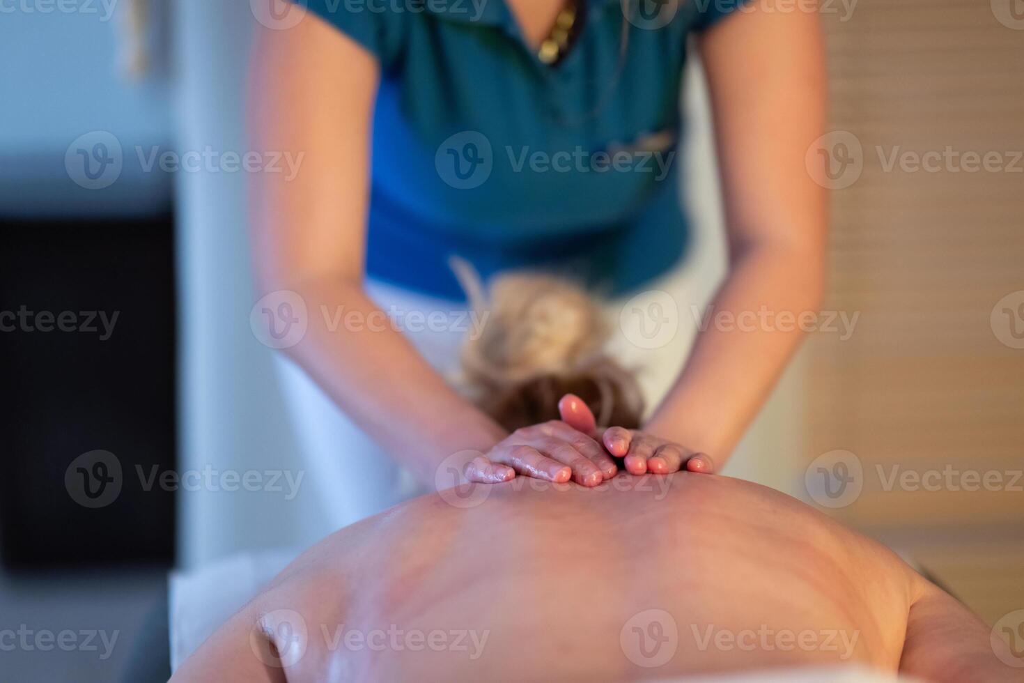 Relaxing Back Massage in a Spa Setting. A professional massage therapist in a blue uniform provides a relaxing back massage to a client lying on a massage table. photo