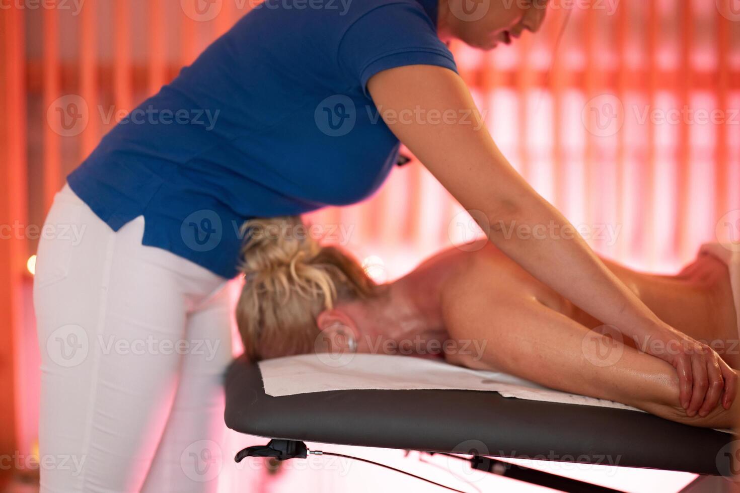 Relaxing Back Massage in a Spa Setting. A professional massage therapist in a blue uniform provides a relaxing back massage to a client lying on a massage table. photo