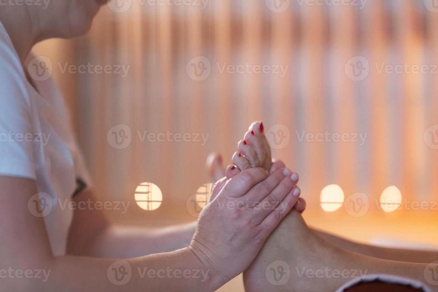 Foot Massage Therapy in a Relaxing Spa Setting. A professional massage therapist in a white uniform provides a soothing foot massage to a client in a calm and serene spa environment photo