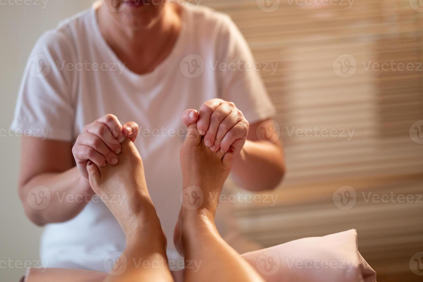 Foot Massage Therapy in a Relaxing Spa Setting. A professional massage therapist in a white uniform provides a soothing foot massage to a client in a calm and serene spa environment photo