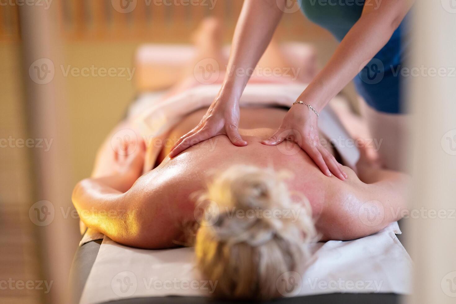 Relaxing Back Massage in a Spa Setting. A professional massage therapist in a blue uniform provides a relaxing back massage to a client lying on a massage table. photo
