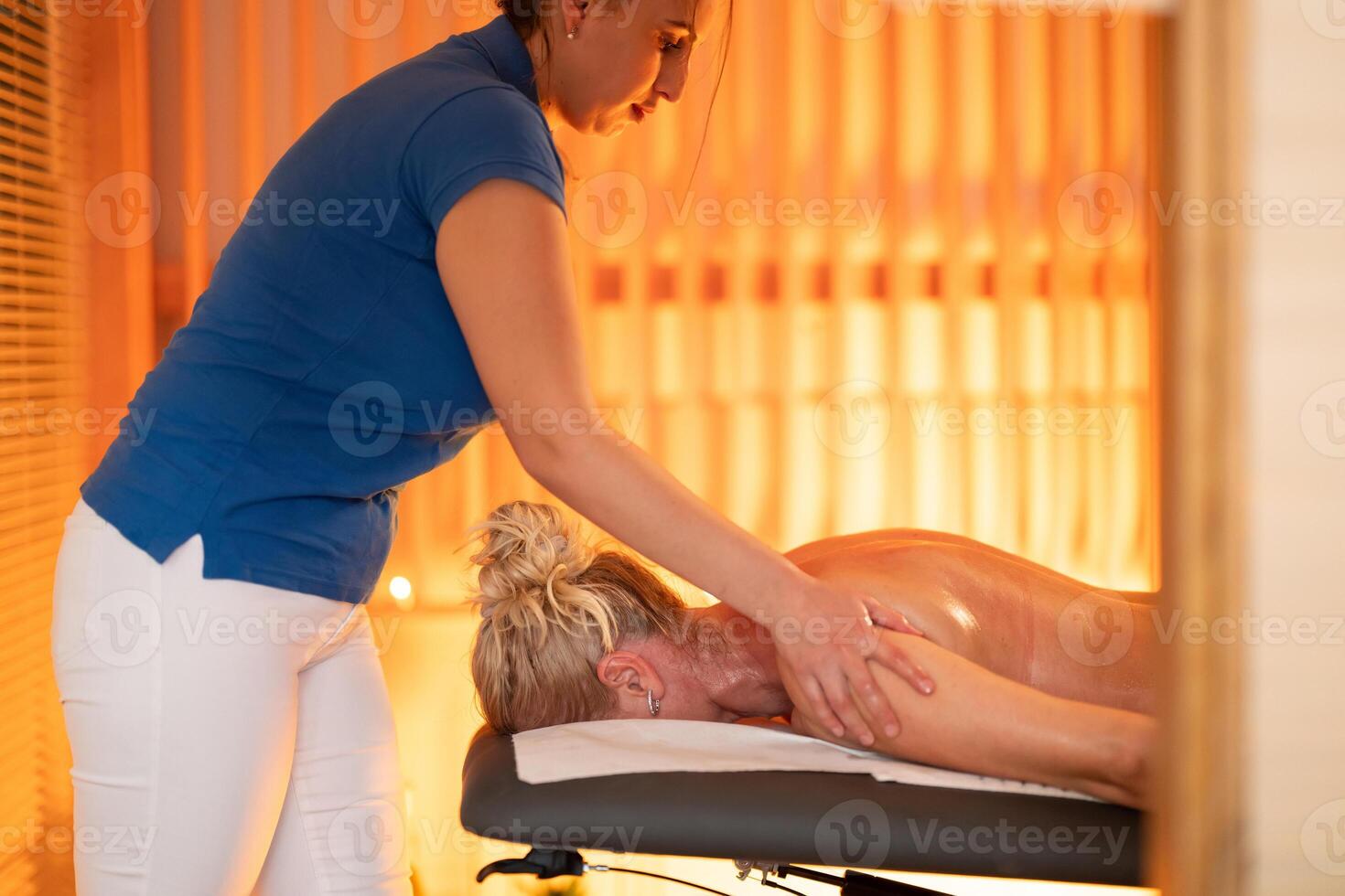 Relaxing Back Massage in a Spa Setting. A professional massage therapist in a blue uniform provides a relaxing back massage to a client lying on a massage table. photo