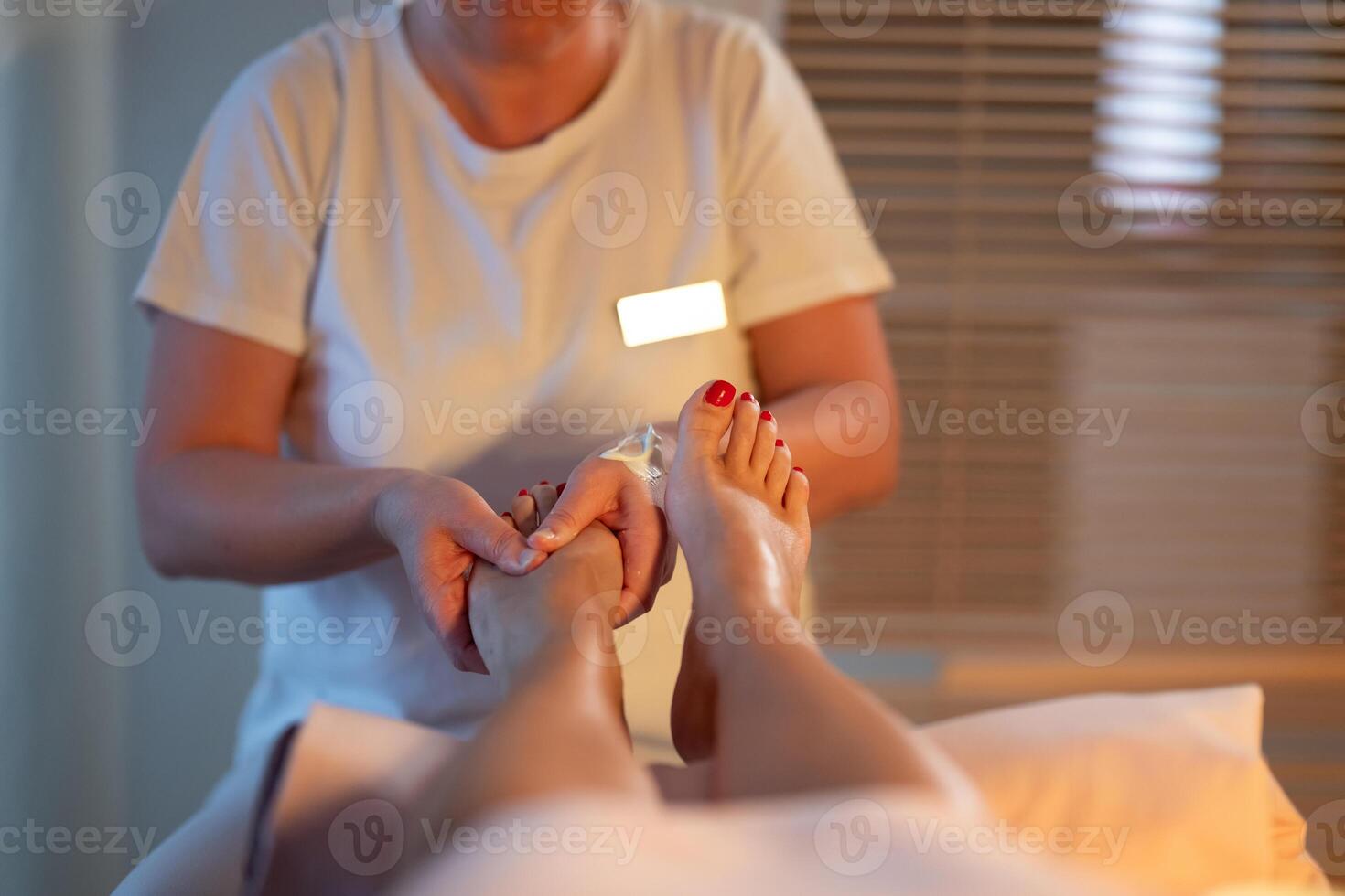 Foot Massage Therapy in a Relaxing Spa Setting. A professional massage therapist in a white uniform provides a soothing foot massage to a client in a calm and serene spa environment photo
