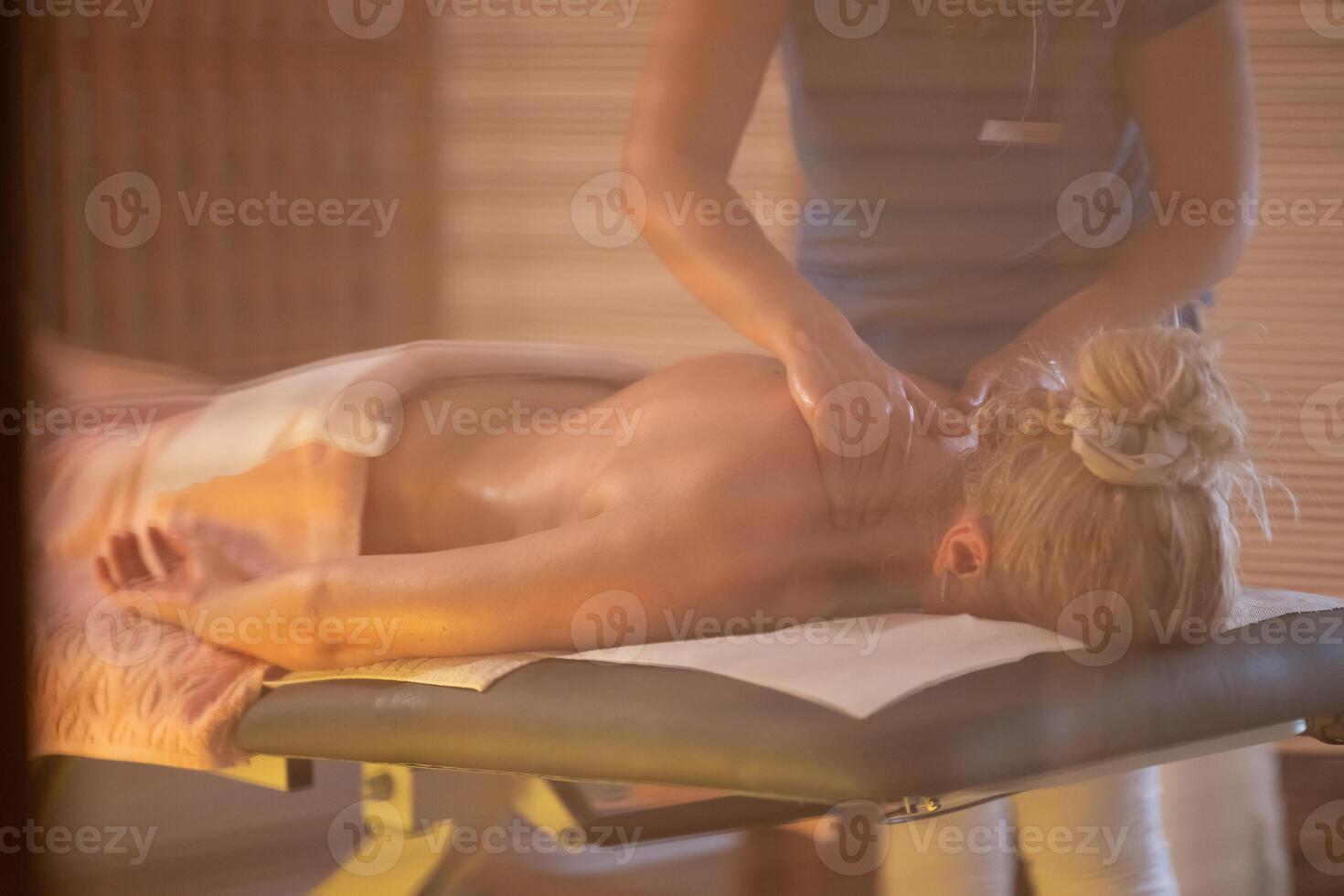 Relaxing Back Massage in a Spa Setting. A professional massage therapist in a blue uniform provides a relaxing back massage to a client lying on a massage table. photo