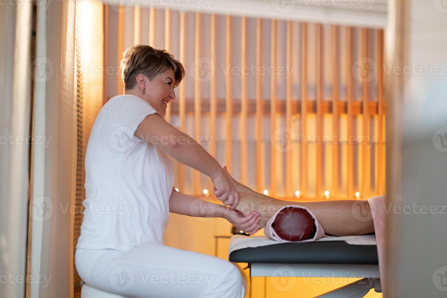 Foot Massage Therapy in a Relaxing Spa Setting. A professional massage therapist in a white uniform provides a soothing foot massage to a client in a calm and serene spa environment photo
