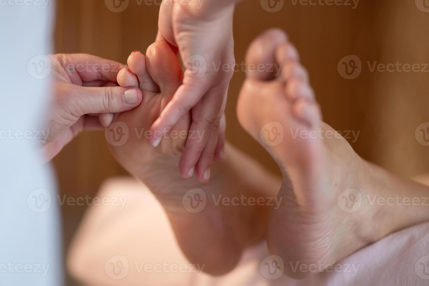 Foot Massage Therapy in a Relaxing Spa Setting. A professional massage therapist in a white uniform provides a soothing foot massage to a client in a calm and serene spa environment photo