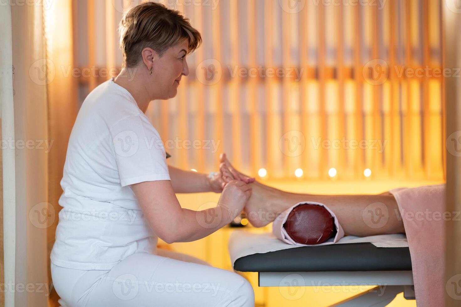 Foot Massage Therapy in a Relaxing Spa Setting. A professional massage therapist in a white uniform provides a soothing foot massage to a client in a calm and serene spa environment photo