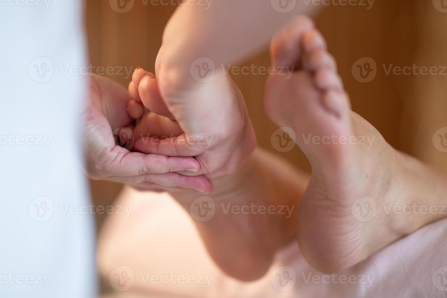 Foot Massage Therapy in a Relaxing Spa Setting. A professional massage therapist in a white uniform provides a soothing foot massage to a client in a calm and serene spa environment photo