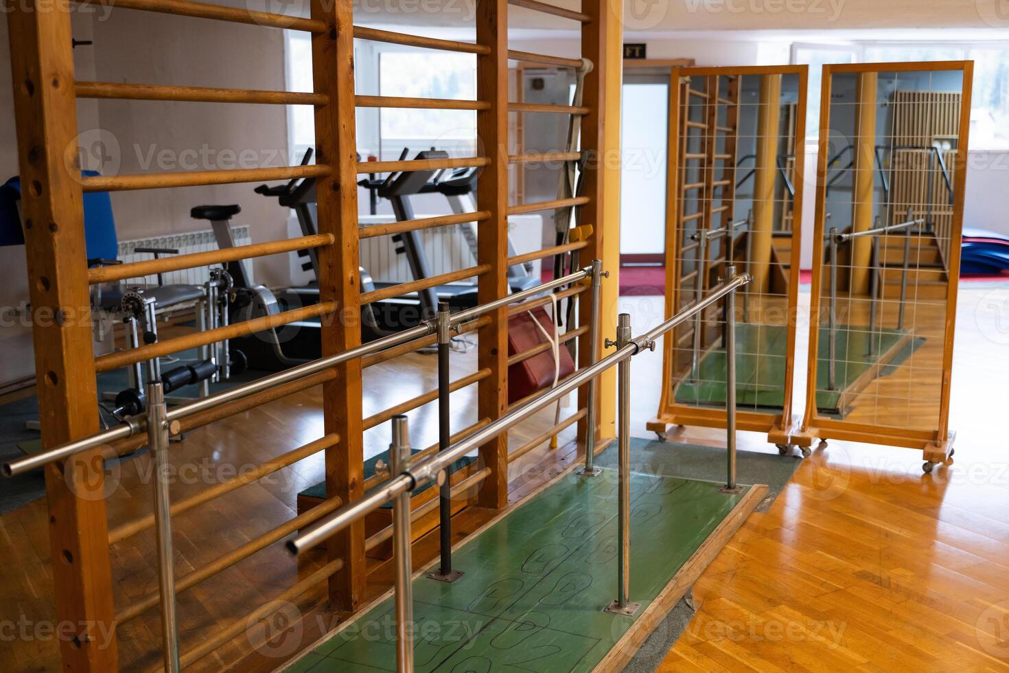 A rehabilitation and physiotherapy gym equipped with parallel bars, wall bars, and mirrors for physical therapy exercises. The space is designed to aid mobility training and recovery. Various exercise photo