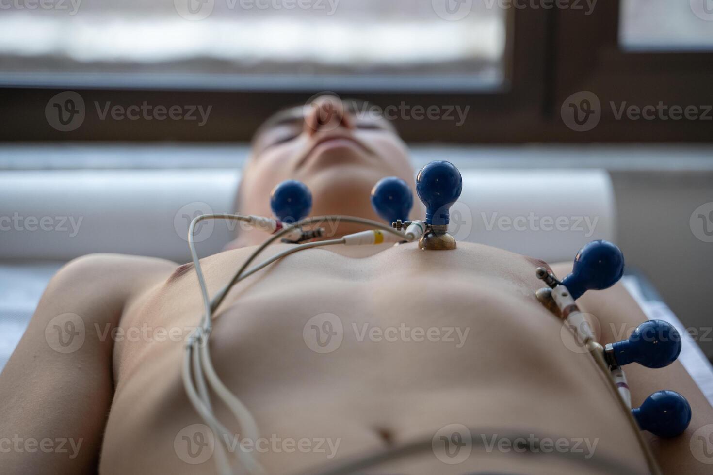 A female doctor performs an ECG on a young man in a hospital room, carefully monitoring his heart health during a routine checkup. photo