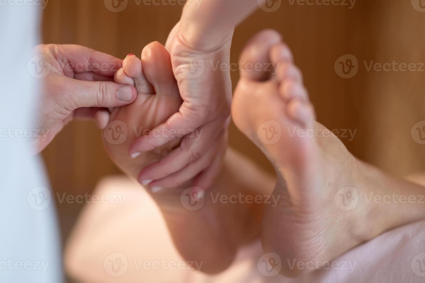 Foot Massage Therapy in a Relaxing Spa Setting. A professional massage therapist in a white uniform provides a soothing foot massage to a client in a calm and serene spa environment photo