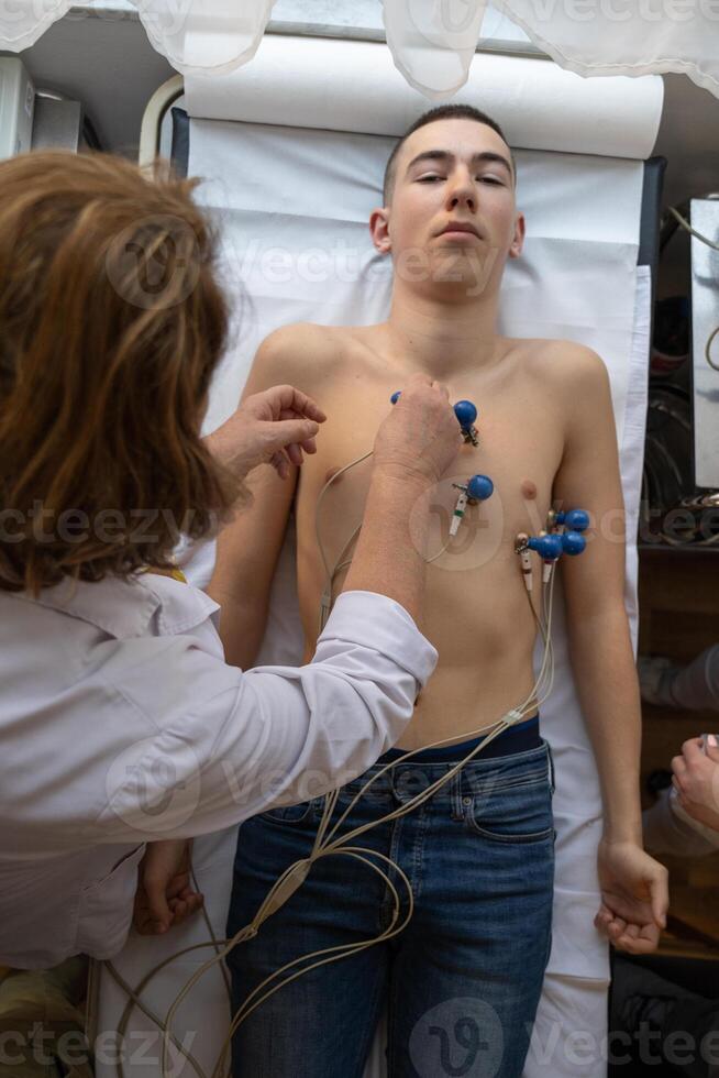 A female doctor performs an ECG on a young man in a hospital room, carefully monitoring his heart health during a routine checkup. photo