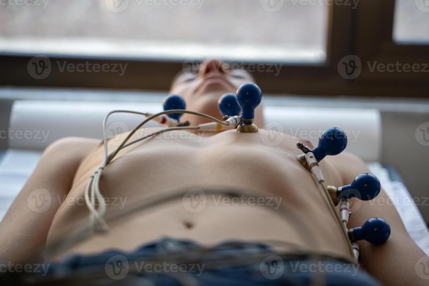 A female doctor performs an ECG on a young man in a hospital room, carefully monitoring his heart health during a routine checkup. photo