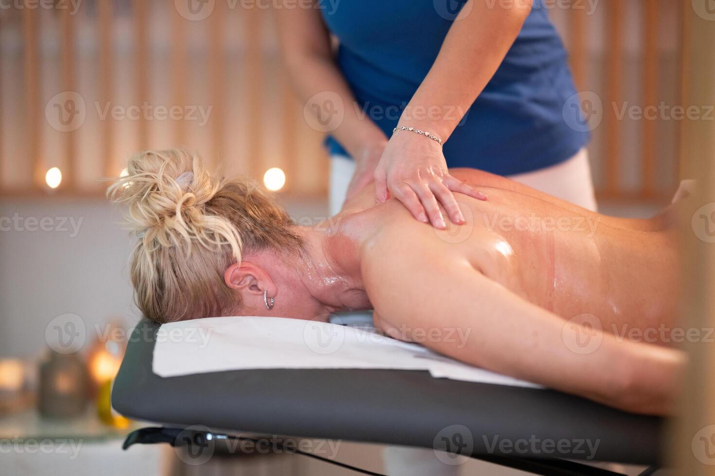 Relaxing Back Massage in a Spa Setting. A professional massage therapist in a blue uniform provides a relaxing back massage to a client lying on a massage table. photo
