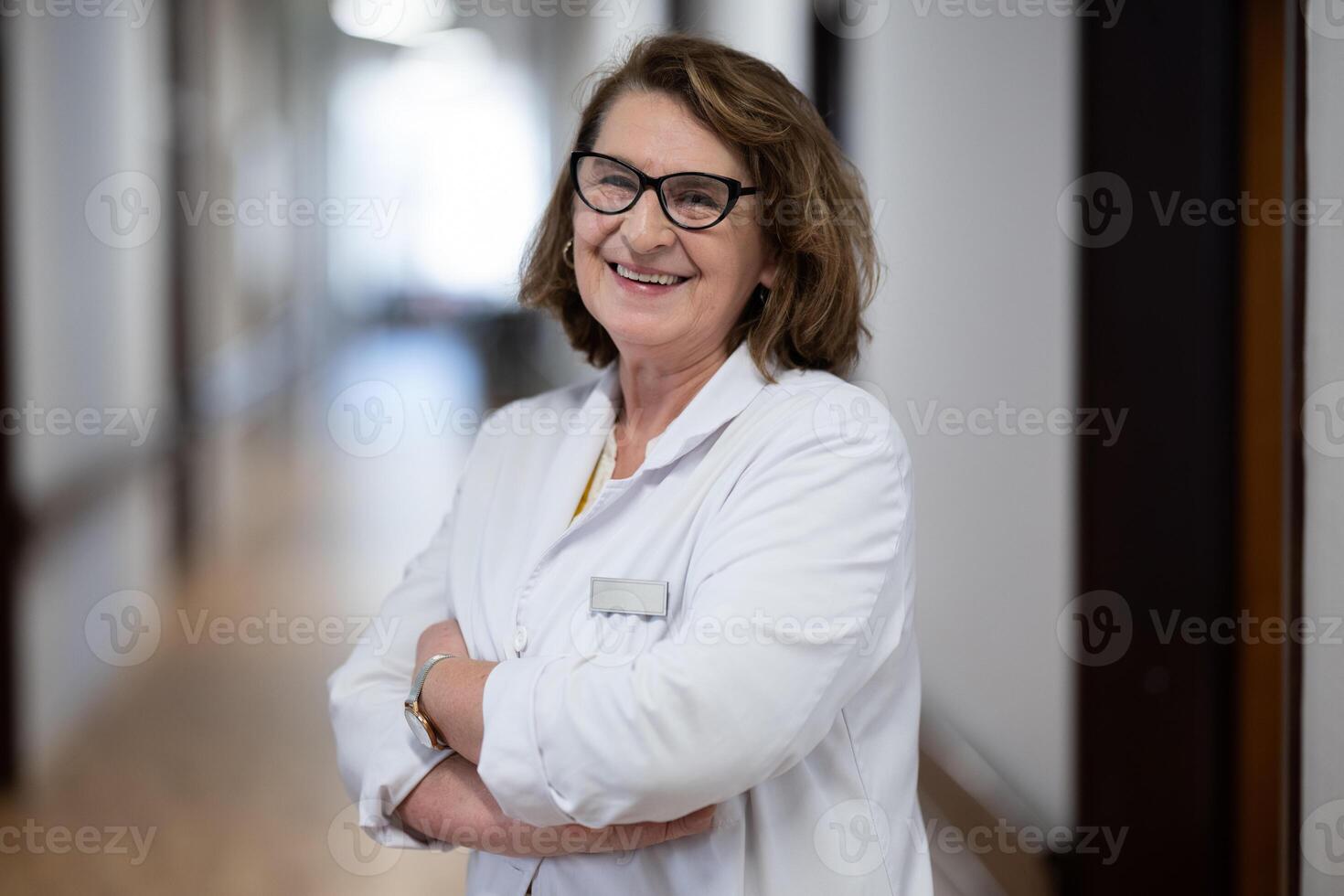 An experienced and confident elderly female doctor, wearing glasses and standing in the hospital hallway, embodies wisdom and dedication to patient care. photo