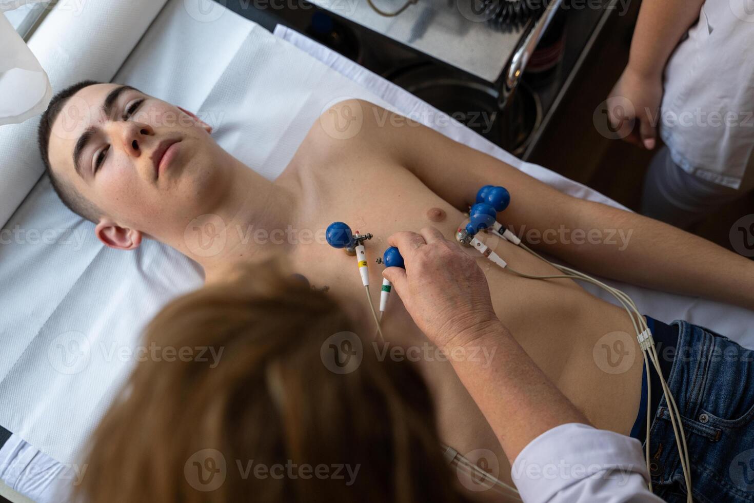 A female doctor performs an ECG on a young man in a hospital room, carefully monitoring his heart health during a routine checkup. photo