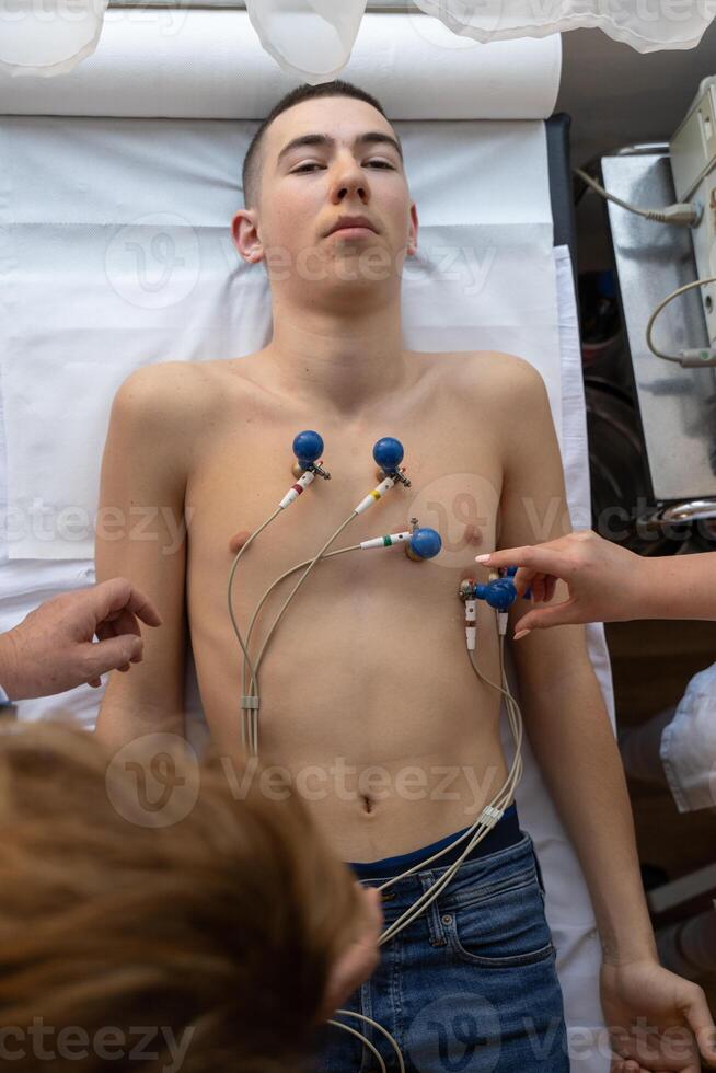 A female doctor performs an ECG on a young man in a hospital room, carefully monitoring his heart health during a routine checkup. photo
