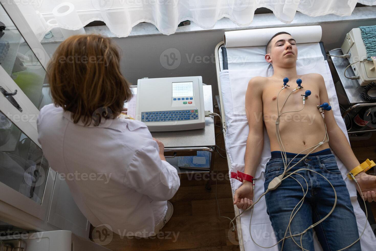 A female doctor performs an ECG on a young man in a hospital room, carefully monitoring his heart health during a routine checkup. photo