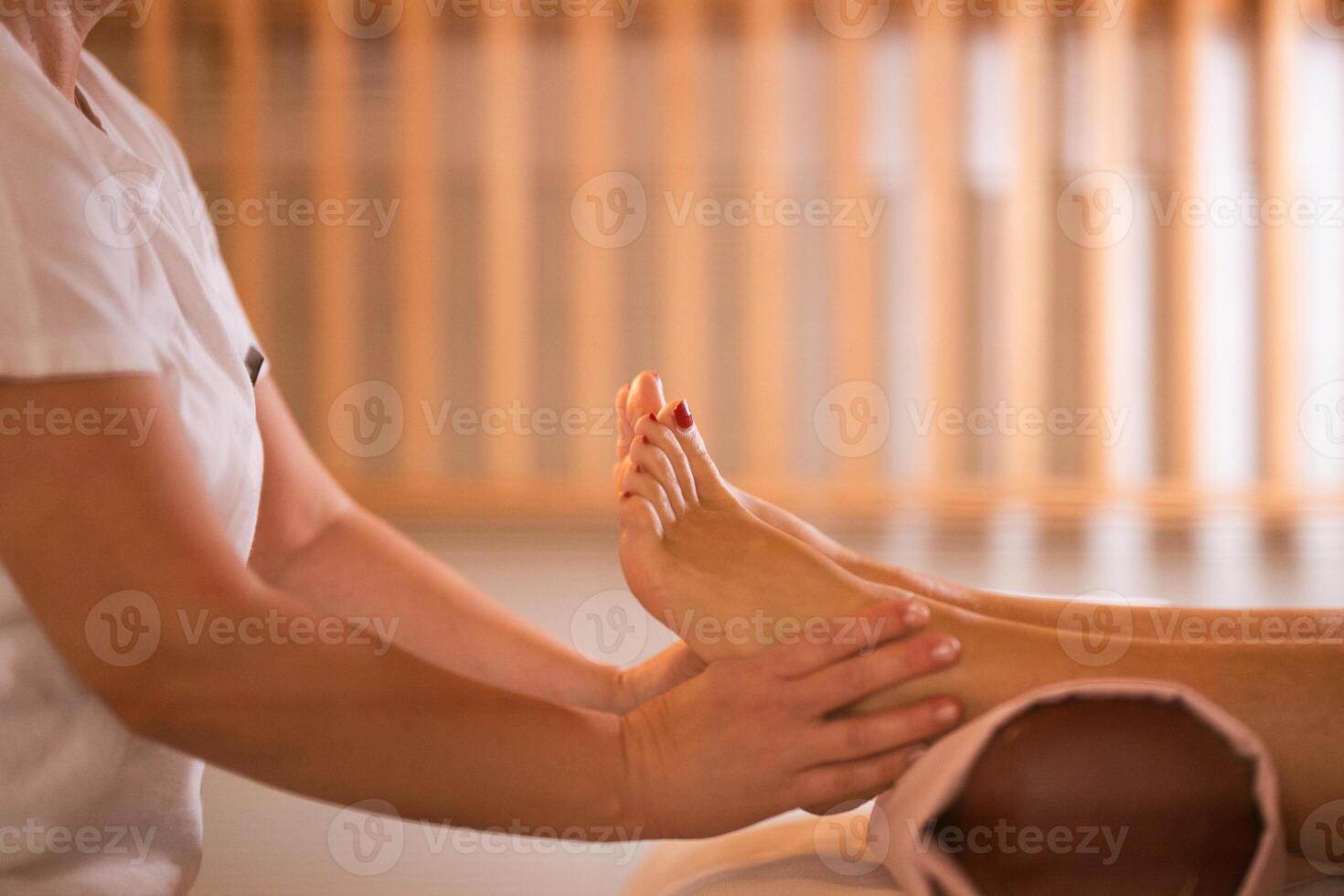Foot Massage Therapy in a Relaxing Spa Setting. A professional massage therapist in a white uniform provides a soothing foot massage to a client in a calm and serene spa environment photo