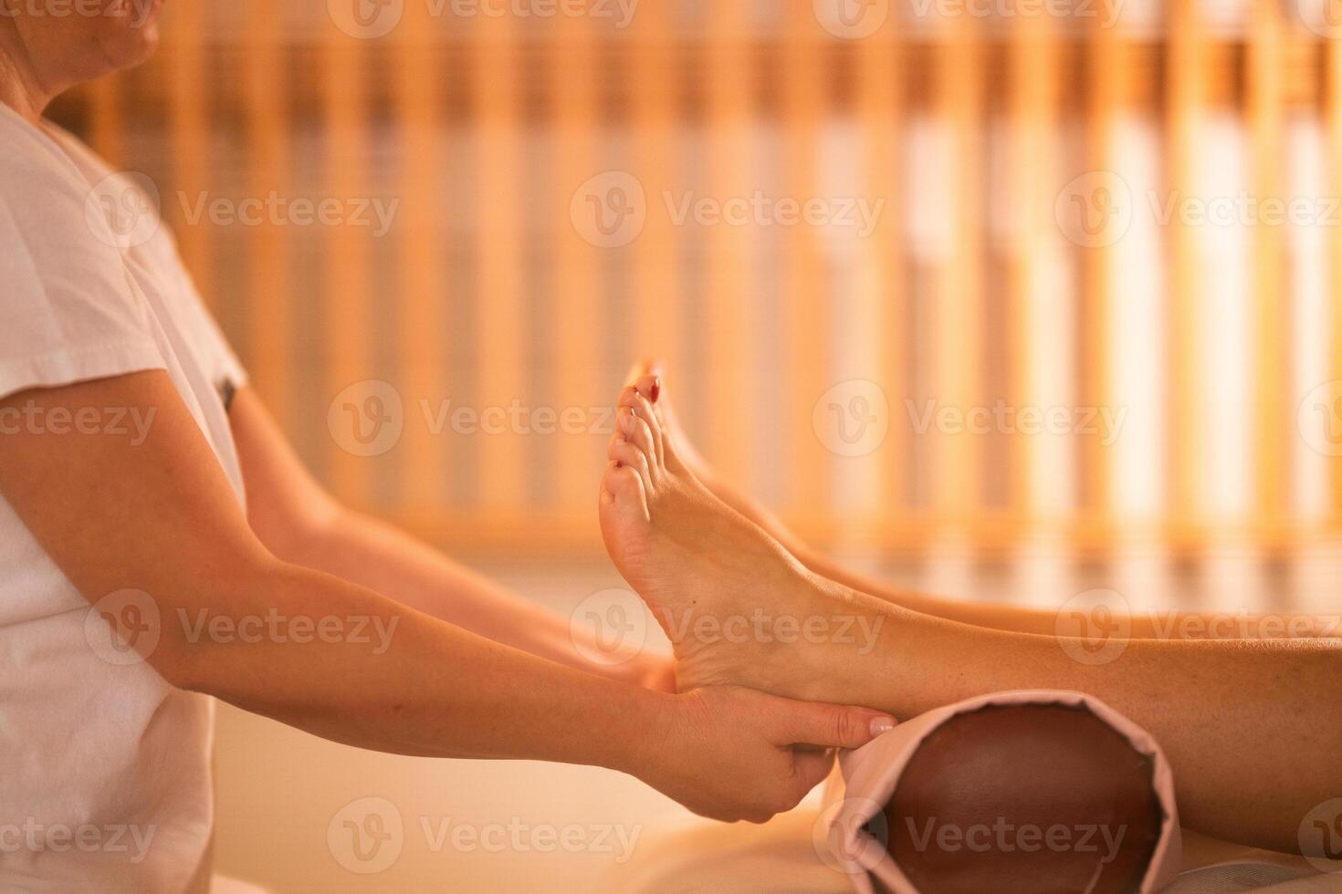 Foot Massage Therapy in a Relaxing Spa Setting. A professional massage therapist in a white uniform provides a soothing foot massage to a client in a calm and serene spa environment photo
