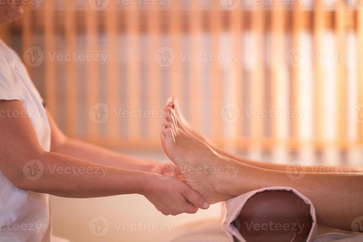 Foot Massage Therapy in a Relaxing Spa Setting. A professional massage therapist in a white uniform provides a soothing foot massage to a client in a calm and serene spa environment photo