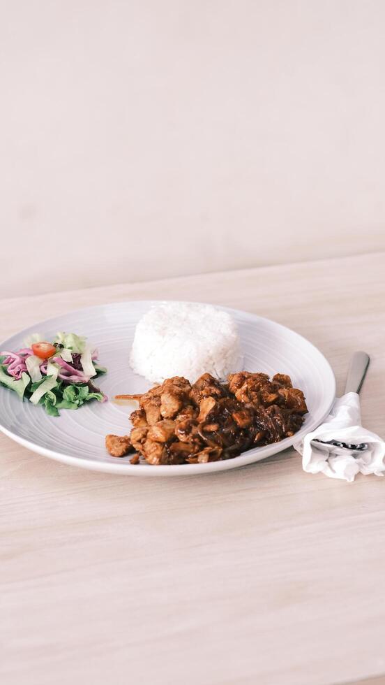 a plate with rice, chicken and salad on a wooden table photo