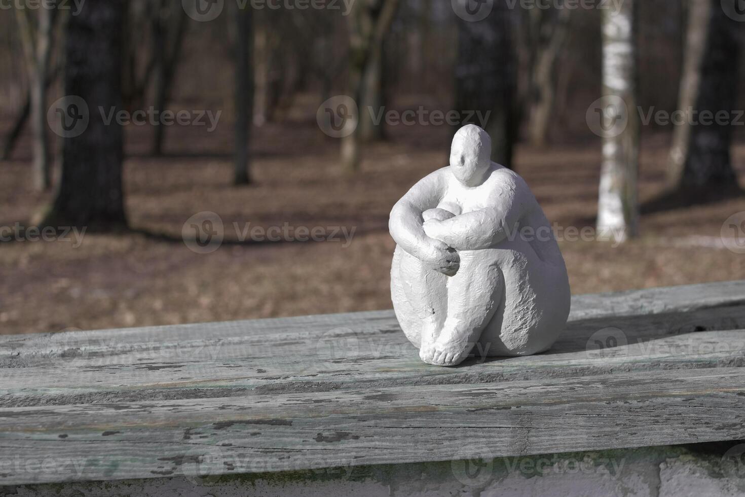 A plaster statue of a full-figured, dreamy woman on a wooden bench in a spring park photo