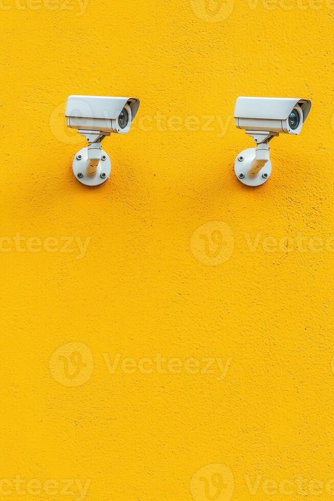 Two surveillance cameras mounted on a vibrant yellow wall, emphasizing security. photo