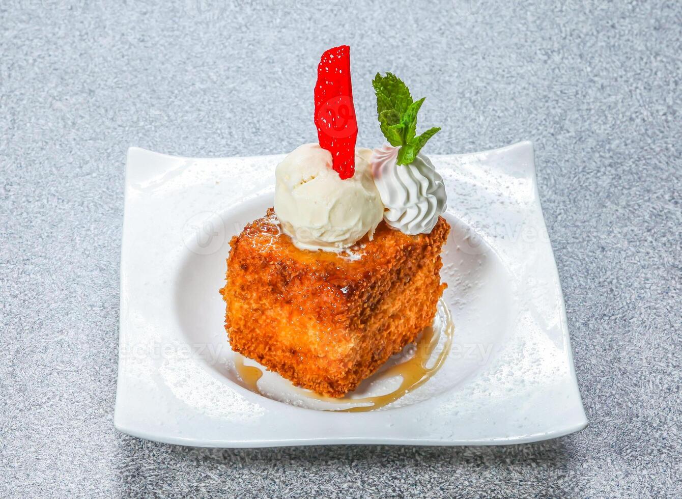 Fried French Toast Cube topped with ice cream, whipped cream, a mint sprig, and red candy served on a plate side view of hong kong food on a textured stone background photo