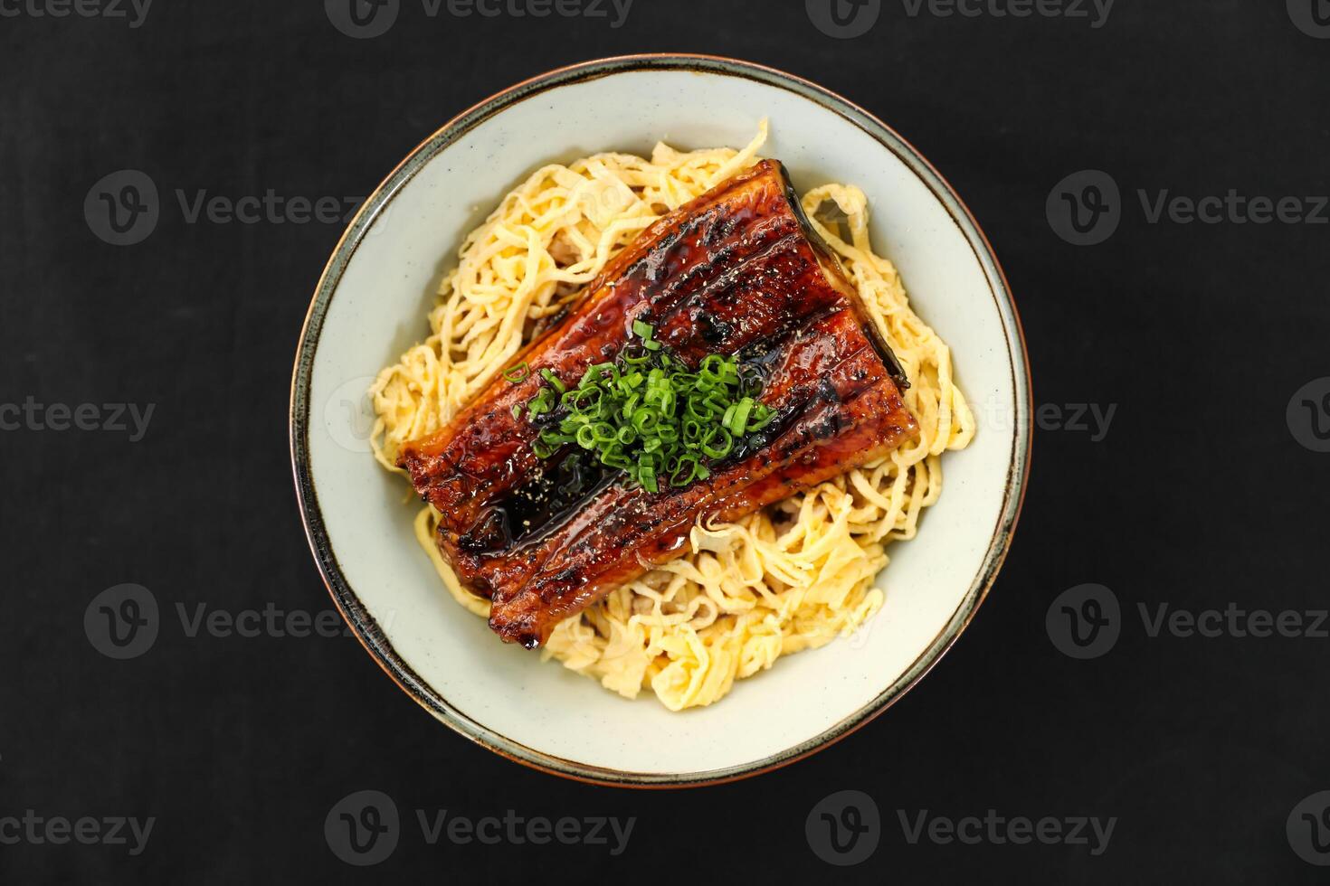 Unagi Don with grilled eel on rice nooldes, garnished with green onions served in bowl isolated on table top view of Japanese cousin photo
