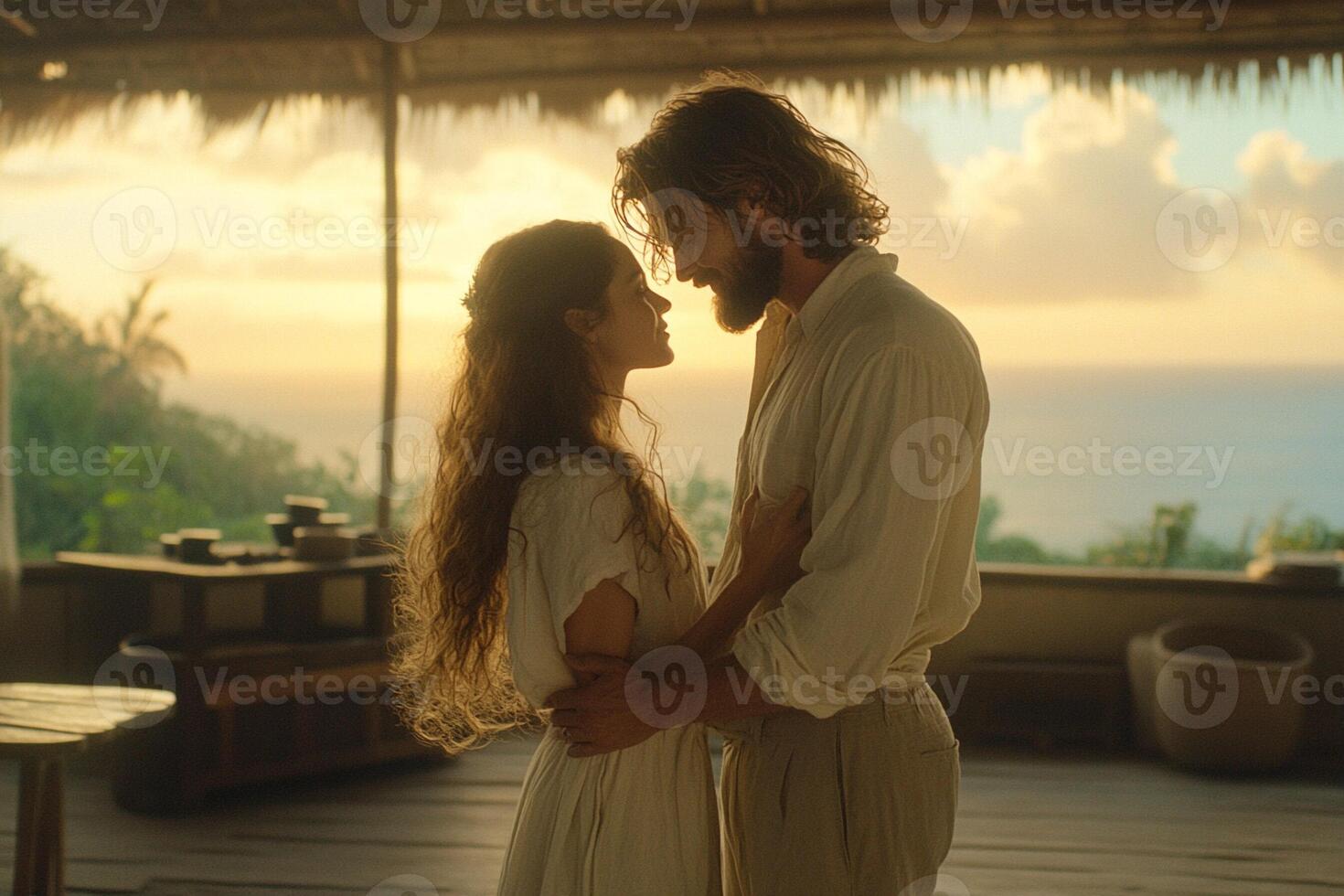 A man and woman standing in front of a hut with the ocean in the background photo
