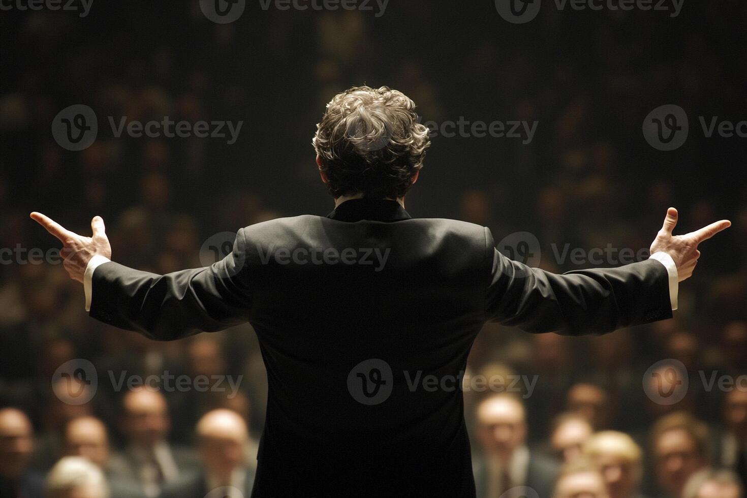 A conductor with his arms outstretched in front of an audience photo