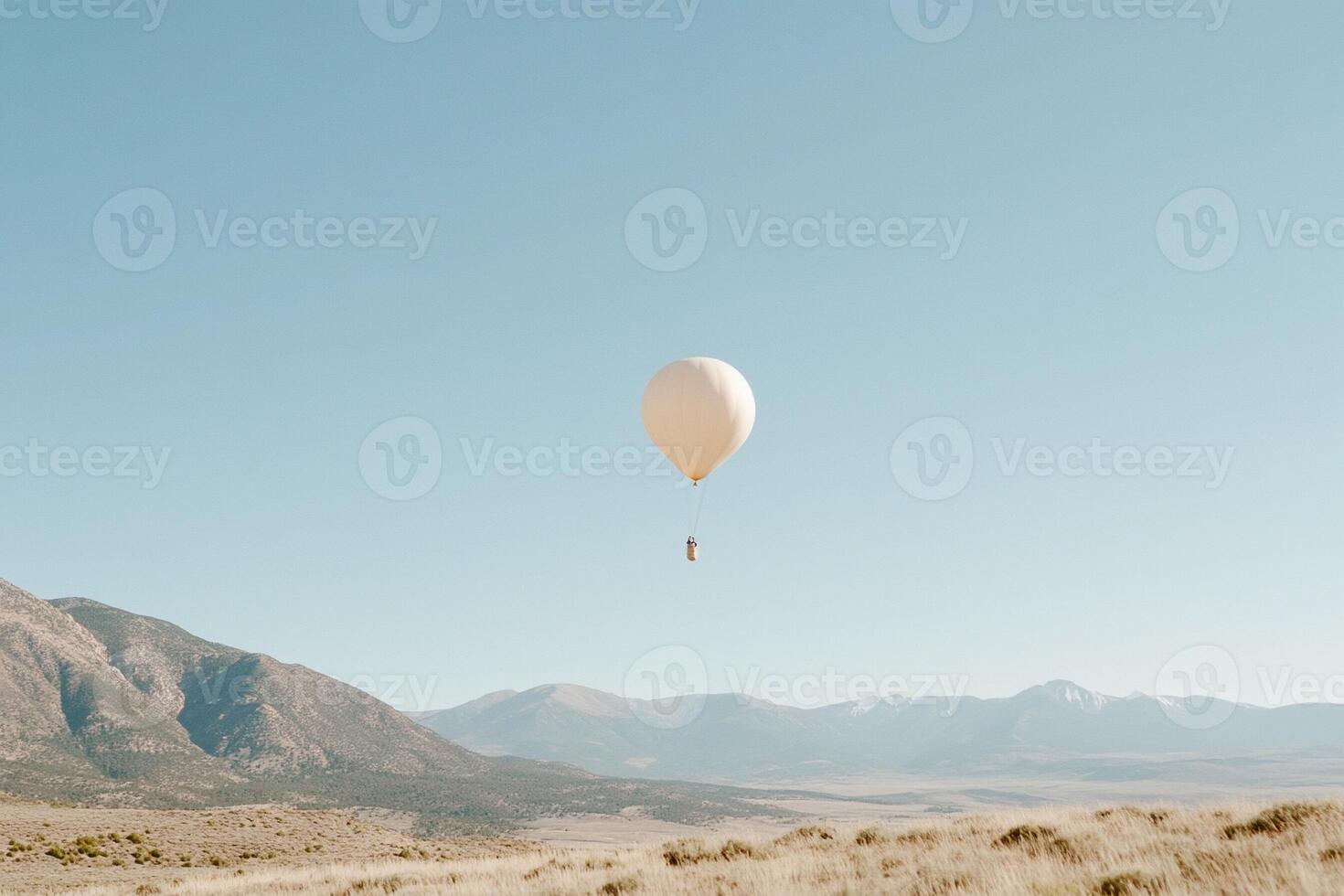 A white balloon flying over a field with mountains in the background photo