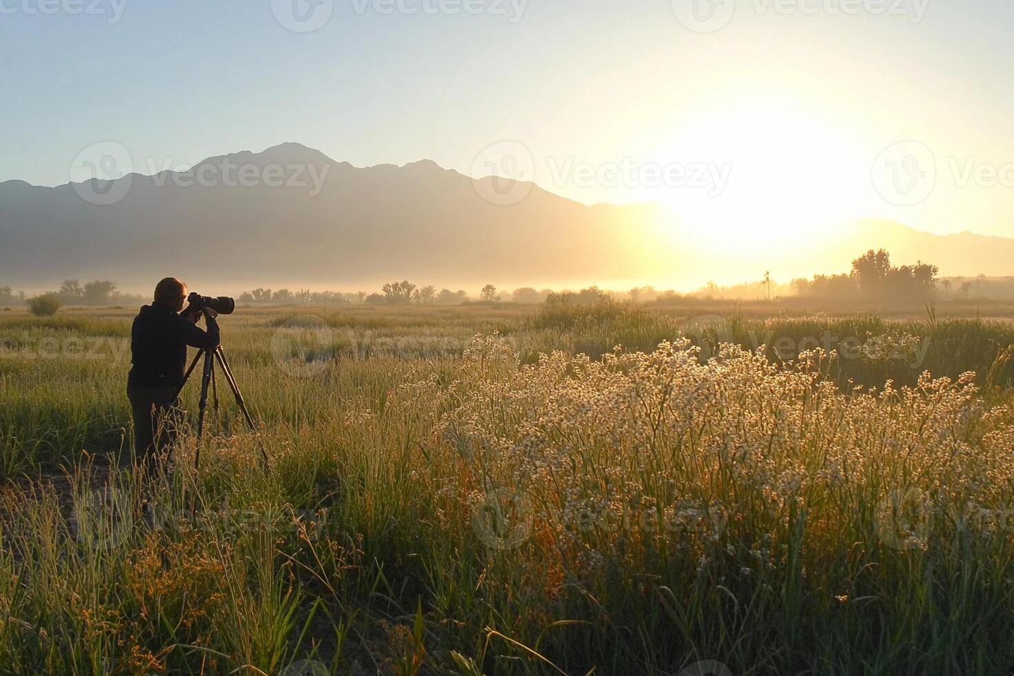 A man taking pictures of the sunrise in a field photo