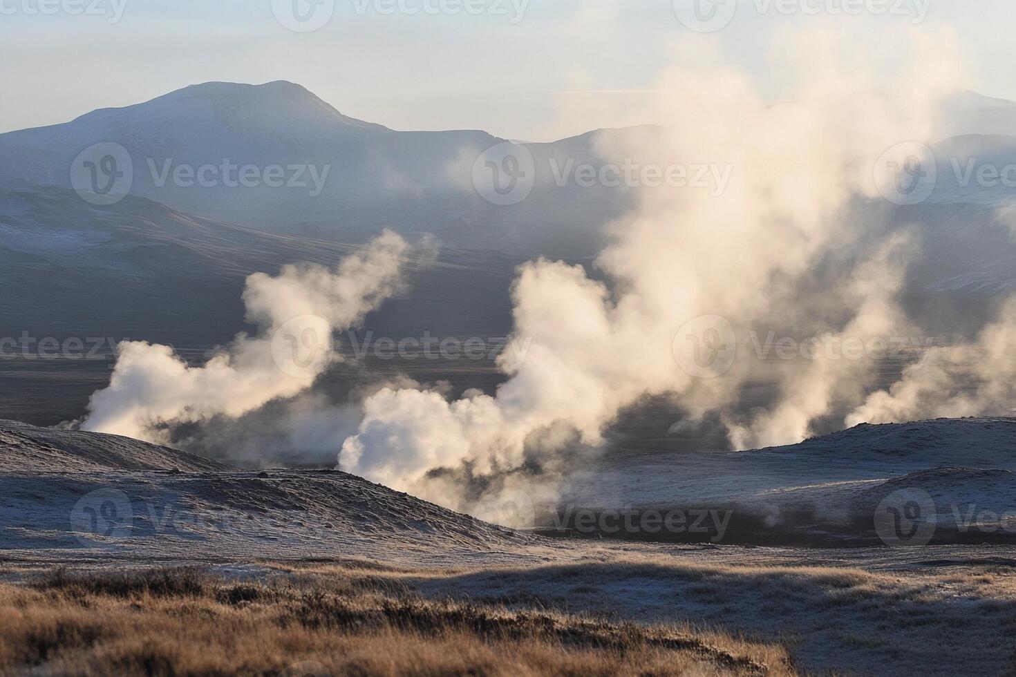 Steam rises from the ground in a field with mountains in the background photo