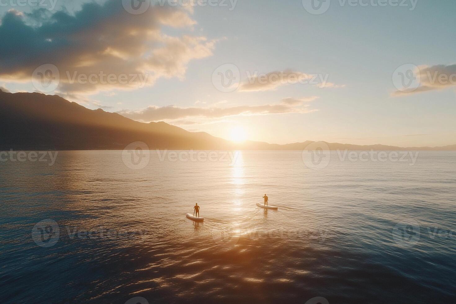 Two people stand up paddle boarding on the ocean at sunset photo