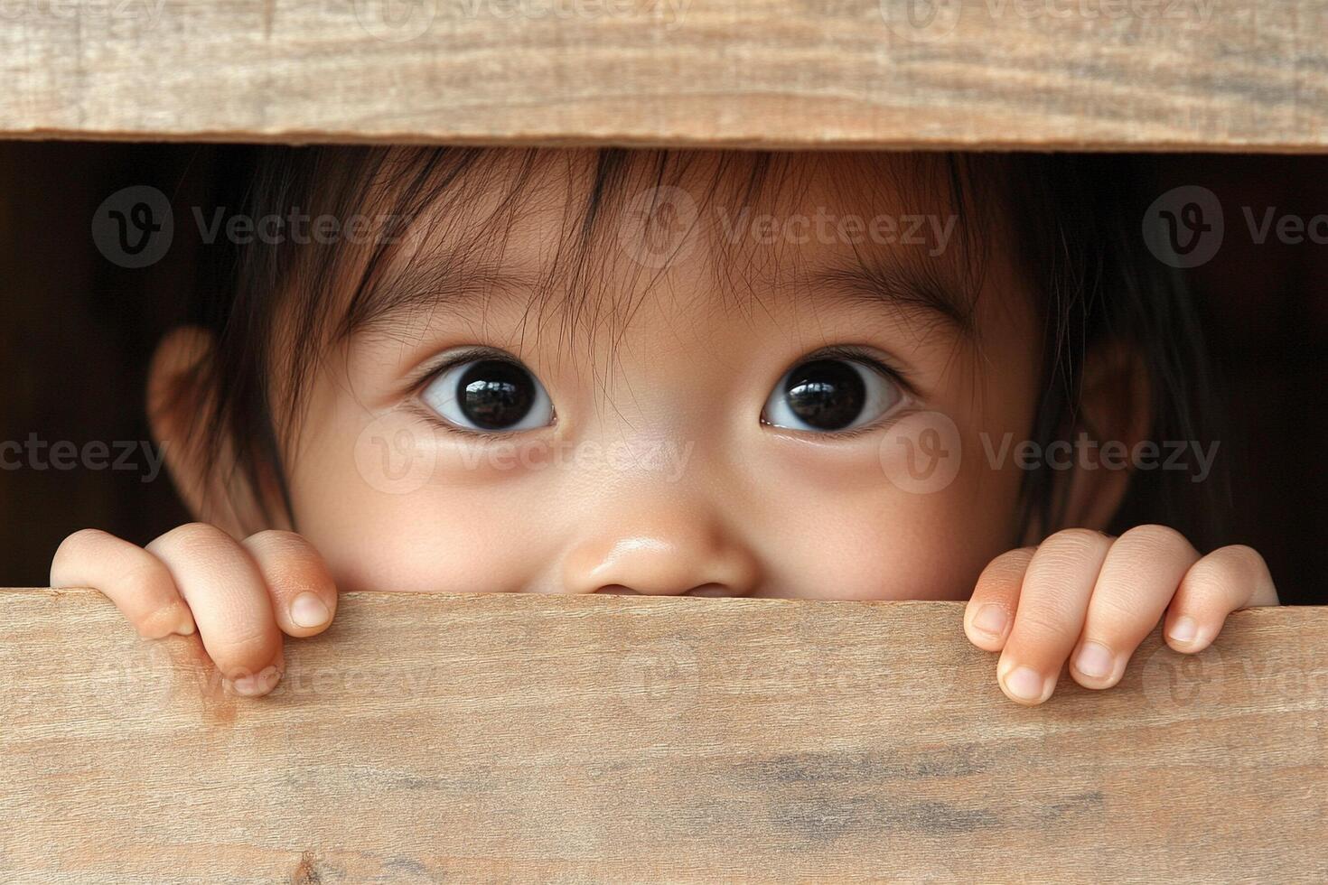 A young child peeking out from behind a wooden box photo