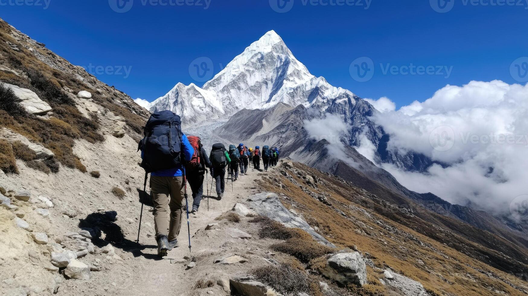 A group of hikers makes their way along a rugged mountain trail, surrounded by impressive snow-capped peaks under a bright blue sky. The trek appears challenging yet invigorating photo
