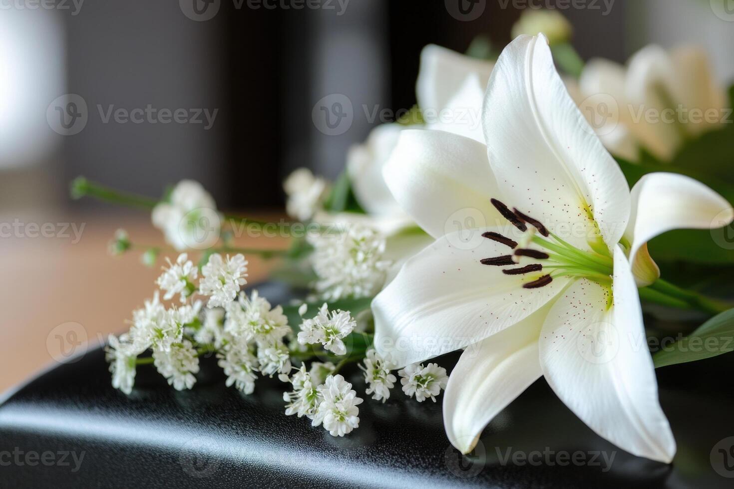 A combination of white lilies and small delicate flowers is thoughtfully placed on a dark surface, creating a poignant tribute at a funeral setting, symbolizing remembrance and peace photo