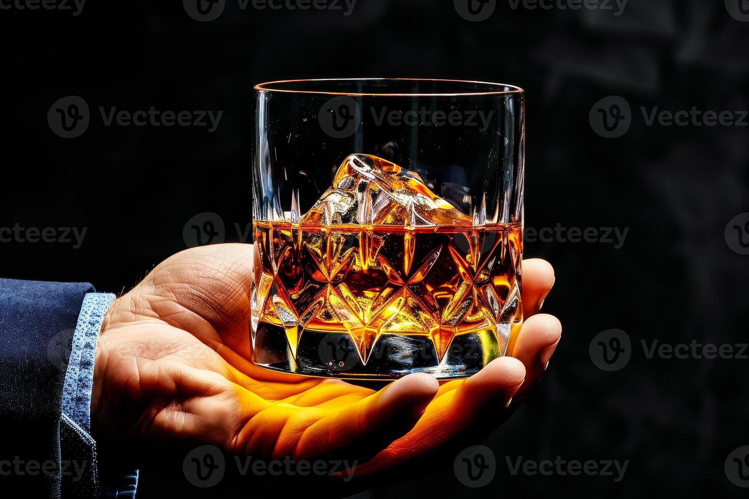 A man holding a glass of whiskey with ice photo