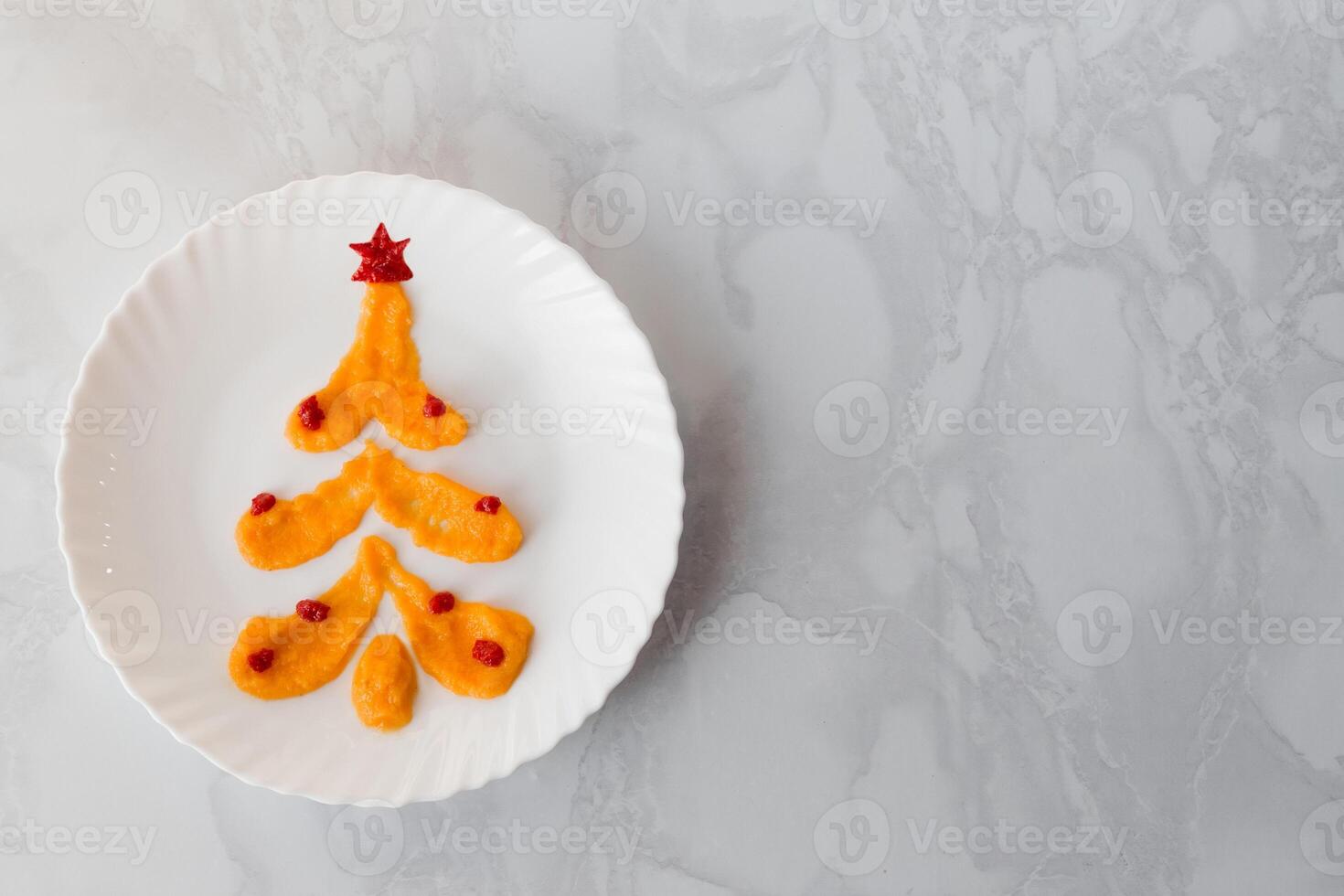 Squash caviar on a white plate in the shape of a Christmas tree decorated with balloons and a ketchup star. Alternative Christmas tree made of food with copy space photo