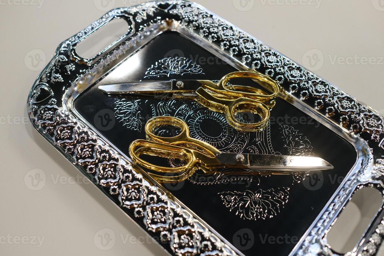 Decorative silver tray showcasing golden-handled scissors resting on an intricately designed surface photo