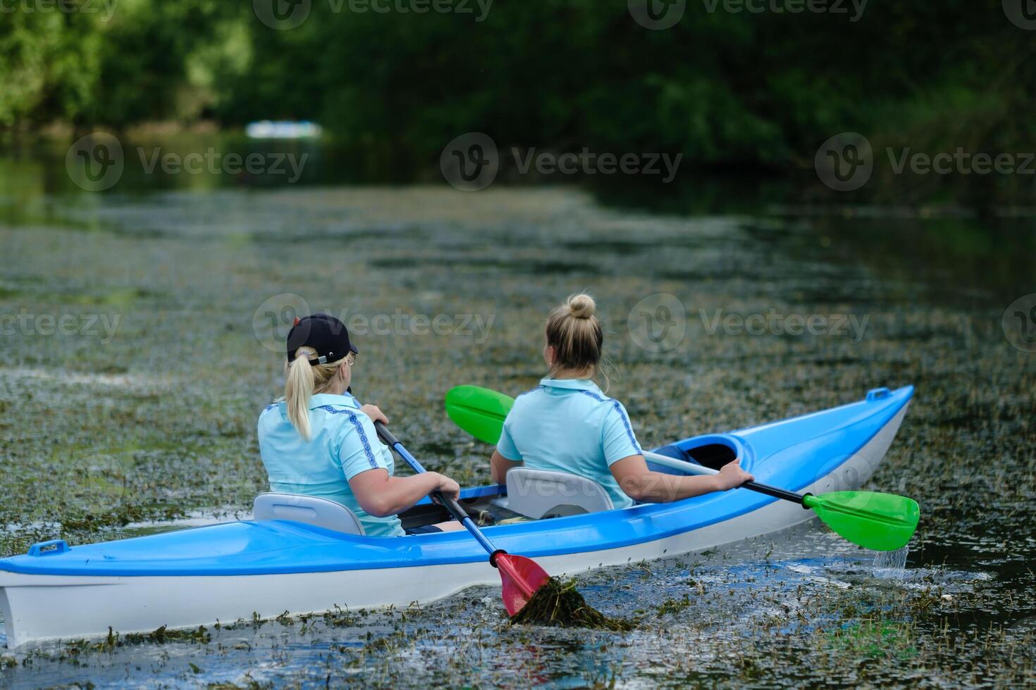 Two women kayaking on a serene river surrounded by lush greenery during a sunny day in summer photo