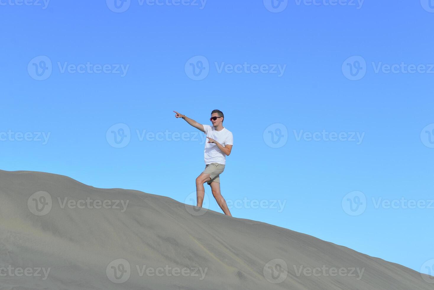 A young man walking along a dune through barkhan in Maspalomas, Gran Canaria on a hot sunny day. A self confident man goes up the mountain - success and achievements concept photo